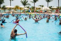 Seorang wanita sedang melakukan gerakan akuarobik di kolam renang, menunjukkan bagaimana olahraga air dapat menjadi pilihan kebugaran yang menyenangkan dan efektif untuk semua usia. Aktivitas ini memanfaatkan daya apung air untuk mengurangi tekanan pada sendi sekaligus memberikan resistensi alami bagi otot.