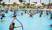 Seorang wanita sedang melakukan gerakan akuarobik di kolam renang, menunjukkan bagaimana olahraga air dapat menjadi pilihan kebugaran yang menyenangkan dan efektif untuk semua usia. Aktivitas ini memanfaatkan daya apung air untuk mengurangi tekanan pada sendi sekaligus memberikan resistensi alami bagi otot.