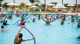 Seorang wanita sedang melakukan gerakan akuarobik di kolam renang, menunjukkan bagaimana olahraga air dapat menjadi pilihan kebugaran yang menyenangkan dan efektif untuk semua usia. Aktivitas ini memanfaatkan daya apung air untuk mengurangi tekanan pada sendi sekaligus memberikan resistensi alami bagi otot.