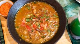 Semangkuk bubur pedas khas Indonesia yang hangat dan kaya rempah, dihiasi dengan irisan telur, bawang goreng, serta kerupuk renyah, siap menggugah selera dan menghadirkan sensasi pedas yang membakar. Hidangan ini memadukan tekstur lembut bubur dengan bumbu pedas yang intens, menciptakan pengalaman makan yang tak terlupakan.