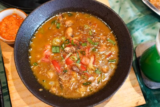 Semangkuk bubur pedas khas Indonesia yang hangat dan kaya rempah, dihiasi dengan irisan telur, bawang goreng, serta kerupuk renyah, siap menggugah selera dan menghadirkan sensasi pedas yang membakar. Hidangan ini memadukan tekstur lembut bubur dengan bumbu pedas yang intens, menciptakan pengalaman makan yang tak terlupakan.