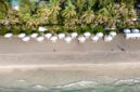 Pemandangan udara pantai pasir putih yang membentang luas, dihiasi dengan air laut biru jernih dan pepohonan kelapa yang melambai, menampilkan pesona alami yang memukau dan menenangkan hati.