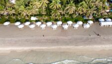 Pemandangan udara pantai pasir putih yang membentang luas, dihiasi dengan air laut biru jernih dan pepohonan kelapa yang melambai, menampilkan pesona alami yang memukau dan menenangkan hati.