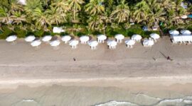 Pemandangan udara pantai pasir putih yang membentang luas, dihiasi dengan air laut biru jernih dan pepohonan kelapa yang melambai, menampilkan pesona alami yang memukau dan menenangkan hati.