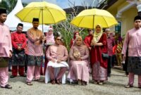 Pasangan pengantin mengenakan busana adat Melayu yang anggun, melambangkan kemewahan dan keindahan tradisi dalam sebuah upacara pernikahan sakral. Pakaian tersebut sering dihiasi sulaman emas atau perak yang menunjukkan kekayaan budaya Melayu.