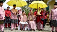 Pasangan pengantin mengenakan busana adat Melayu yang anggun, melambangkan kemewahan dan keindahan tradisi dalam sebuah upacara pernikahan sakral. Pakaian tersebut sering dihiasi sulaman emas atau perak yang menunjukkan kekayaan budaya Melayu.