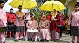 Pasangan pengantin mengenakan busana adat Melayu yang anggun, melambangkan kemewahan dan keindahan tradisi dalam sebuah upacara pernikahan sakral. Pakaian tersebut sering dihiasi sulaman emas atau perak yang menunjukkan kekayaan budaya Melayu.