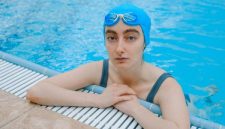 Seorang wanita melakukan gerakan aqua aerobic dengan riang di dalam kolam renang, menunjukkan bagaimana olahraga air bisa menjadi aktivitas kebugaran yang menyenangkan dan menyegarkan. Latihan di dalam air mengurangi beban pada sendi sekaligus memberikan resistensi alami untuk melatih otot secara efektif.