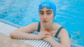Seorang wanita melakukan gerakan aqua aerobic dengan riang di dalam kolam renang, menunjukkan bagaimana olahraga air bisa menjadi aktivitas kebugaran yang menyenangkan dan menyegarkan. Latihan di dalam air mengurangi beban pada sendi sekaligus memberikan resistensi alami untuk melatih otot secara efektif.