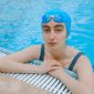Seorang wanita melakukan gerakan aqua aerobic dengan riang di dalam kolam renang, menunjukkan bagaimana olahraga air bisa menjadi aktivitas kebugaran yang menyenangkan dan menyegarkan. Latihan di dalam air mengurangi beban pada sendi sekaligus memberikan resistensi alami untuk melatih otot secara efektif.