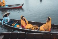 Perahu tradisional melintasi aliran Sungai Kapuas yang tenang, dikelilingi rimbunnya hutan hujan tropis Kalimantan, menunjukkan harmoni antara manusia dan alam.