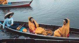 Perahu tradisional melintasi aliran Sungai Kapuas yang tenang, dikelilingi rimbunnya hutan hujan tropis Kalimantan, menunjukkan harmoni antara manusia dan alam.