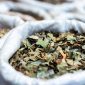 Seorang wanita sedang meracik ramuan herbal tradisional Melayu menggunakan aneka rempah dan dedaunan segar, menunjukkan proses otentik pembuatan jamu. Gambar ini menggambarkan kekayaan bahan alami yang menjadi dasar pengobatan turun-temurun.
