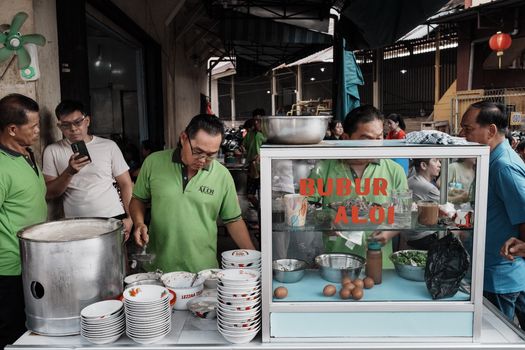 Semangkuk bubur pedas khas Pontianak dengan taburan kacang, ikan teri, dan irisan sayuran hijau, siap menggugah selera dengan cita rasa rempah yang kaya dan pedasnya yang menghangatkan. Hidangan ini merupakan perpaduan sempurna antara kelembutan bubur dan kekuatan bumbu tradisional Indonesia.